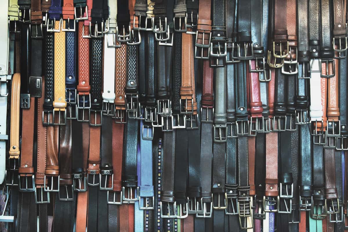 A leather belt with a metal buckle laid flat on a neutral surface