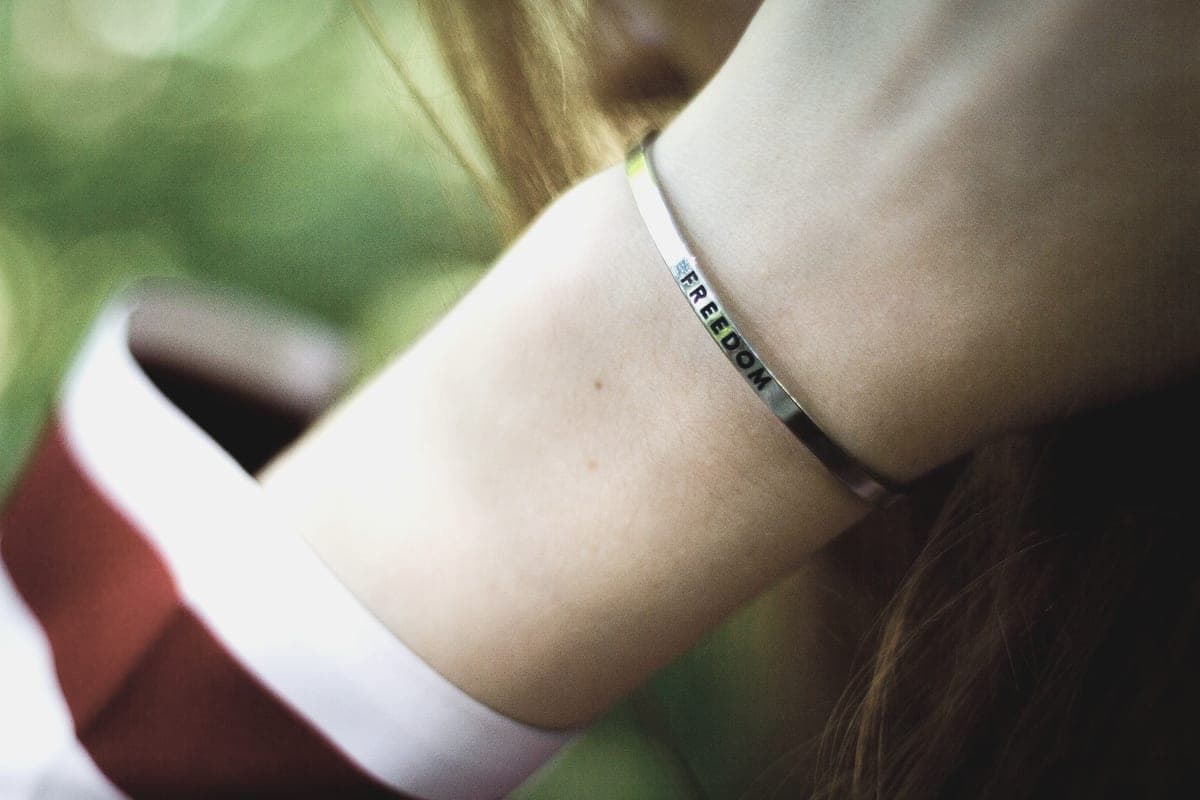 A narrow engraved metal cuff bracelet worn on a wrist
