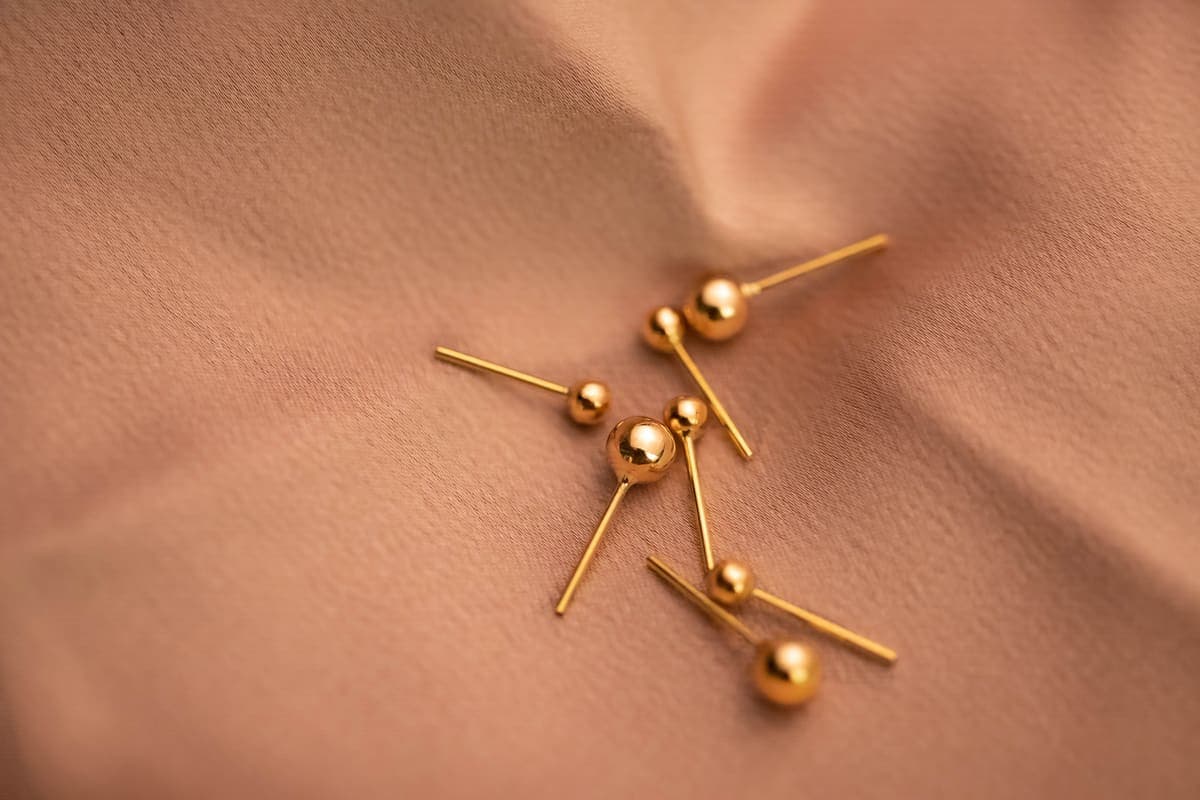 Small gold-toned ball stud earrings arranged on soft pale fabric