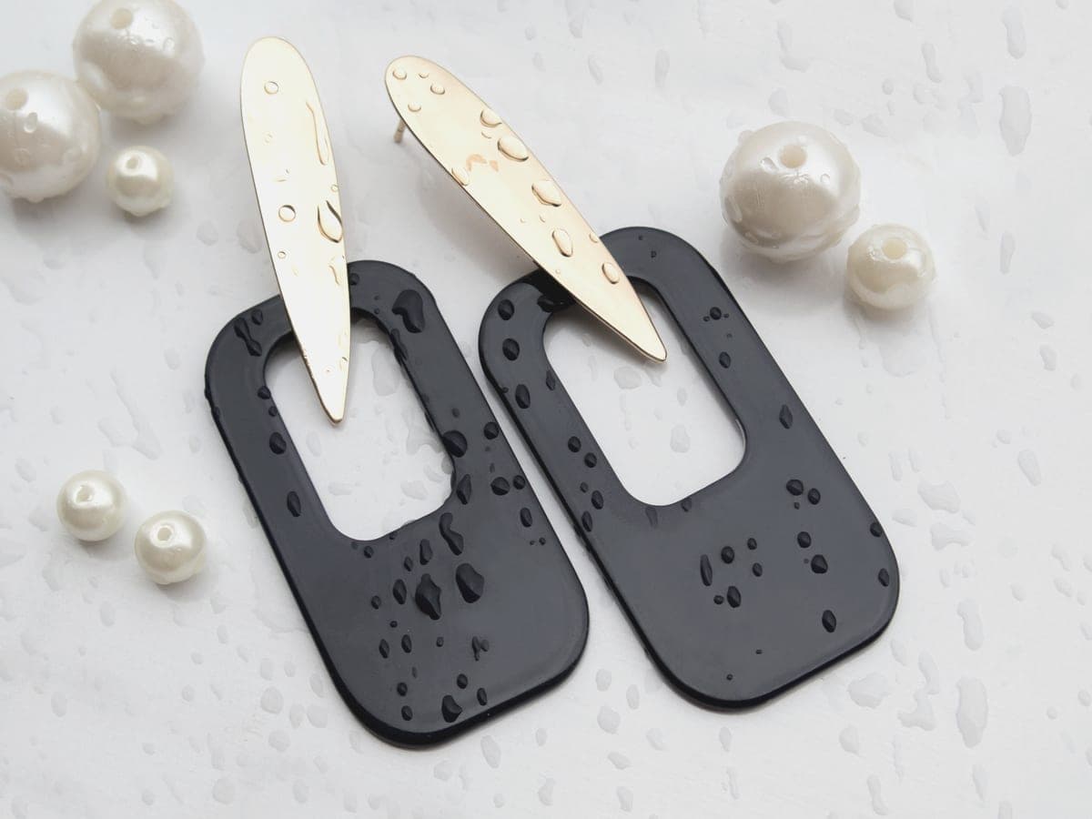 Water droplets beside jewelry on a pale, softly lit surface
