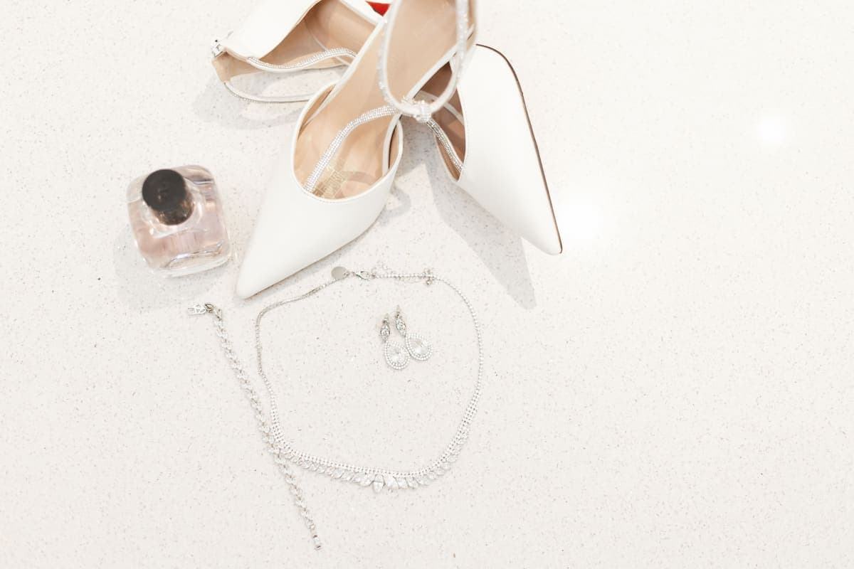 Bridal shoes, jewelry and a perfume bottle arranged on a pale surface